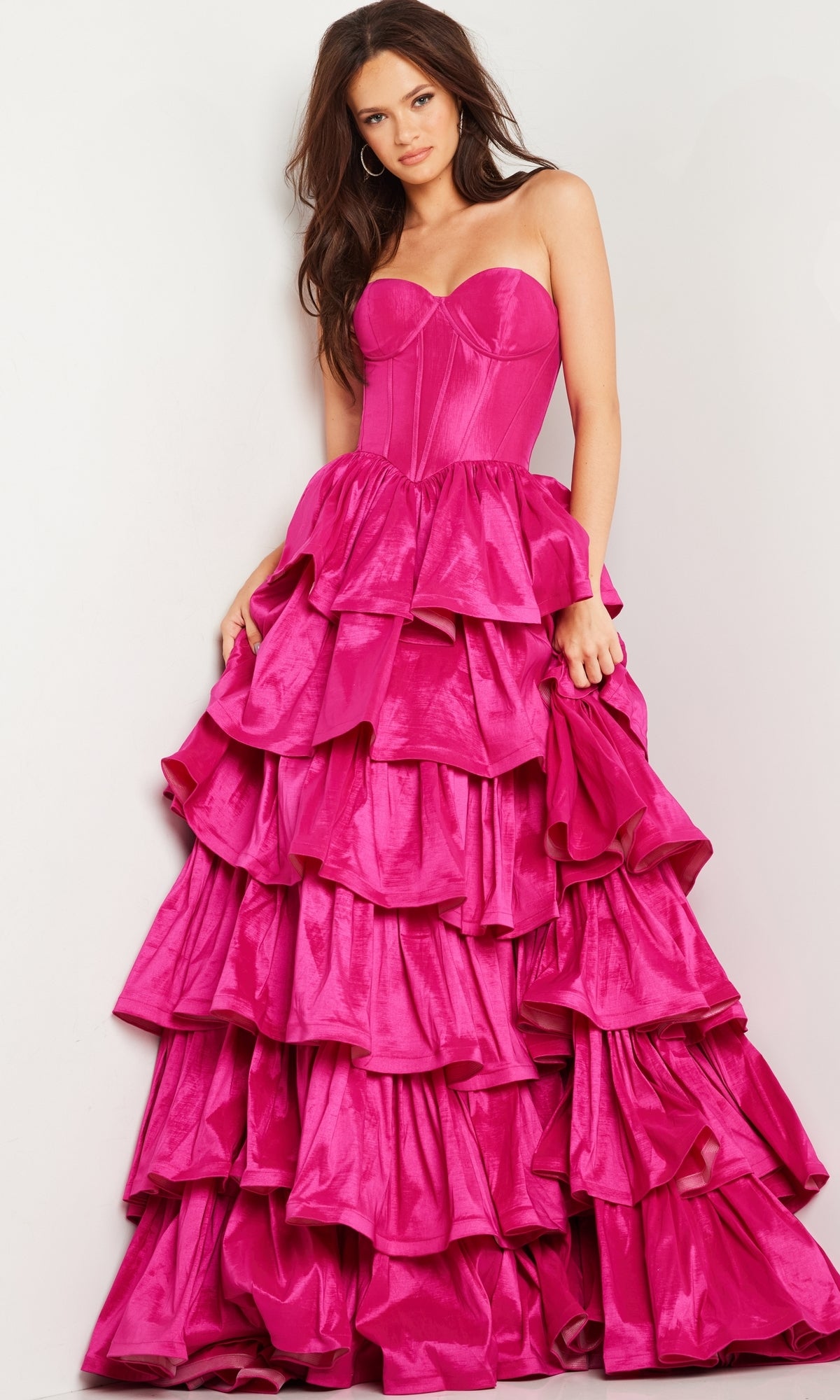 A woman models the Strapless Ruffled Prom Ball Gown: Jovani 36619, showcasing a bright pink fitted bodice and a skirt with multiple tiered ruffle layers, set against a plain background.